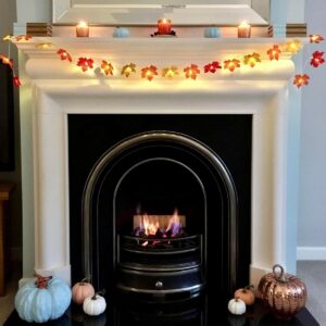 Autumn leaves LED light garland hung over fireplace surrounded by pumpkins