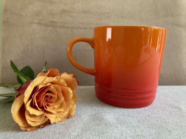 Orange Le Crueset mug next to orange rose