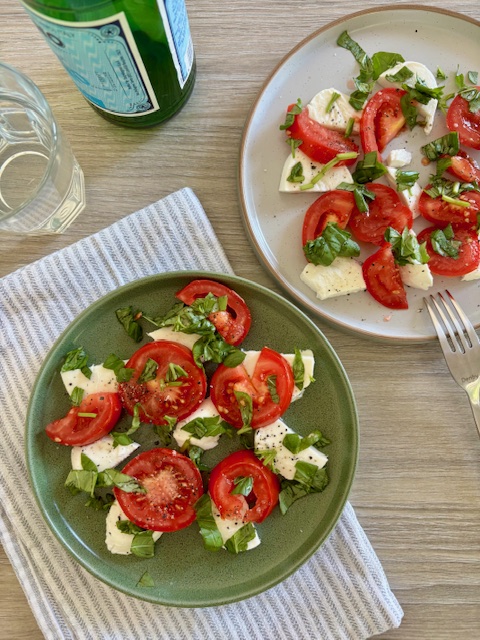 Two plates of tomato and mozzarella salad next to a fork and glass of water