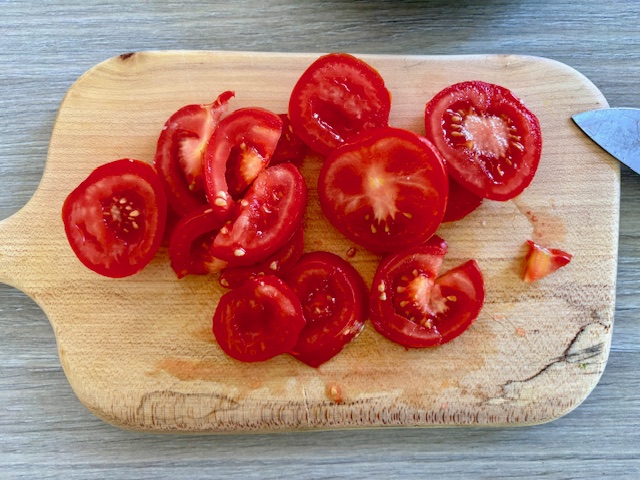 Tomato slices on a wooden chopping board next to a knife