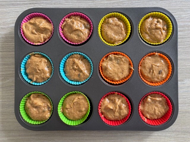 Banana chocolate chip muffin mixture split into 12 silicone muffin cases placed in baking pan