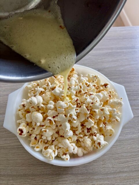 Pouring melted butter over the popcorn in a mixing bowl