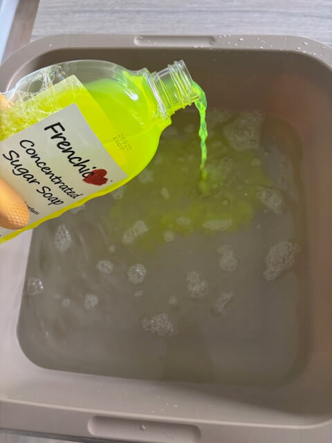 Pouring sugar soap into a washing up bowl filled with water