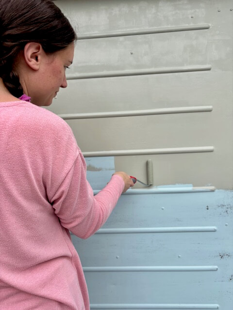 Woman applying first coat of paint on to garage door using a paint roller