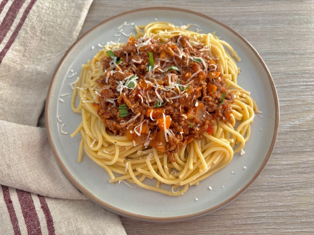 Bolognese sauce served on top of spaghetti with grated cheese and fresh basil on top.