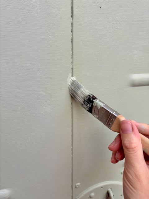 Hand holding a paint brush applying paint into groove of garage door.