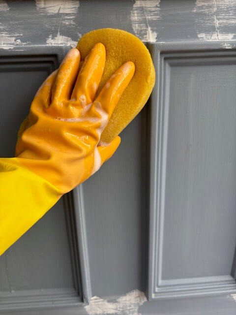 Gloved hand using a sponge to apply the sugar soap to the front door