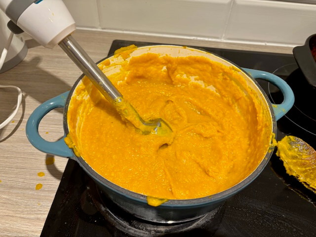 Using a handheld immersion blender to blend the soup.