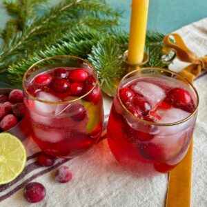 Cranberry Fizz Mocktails served in gold rimmed glass tumblers, garnished with ice and frozen cranberries.