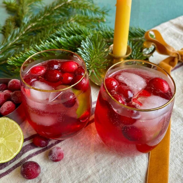 Cranberry Fizz Mocktails served in gold rimmed glass tumblers, garnished with ice and frozen cranberries.