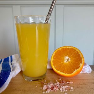 Homemade Electrolyte Drink in glass next to orange cut in half and a small pile Pink Himalayan salt granules.