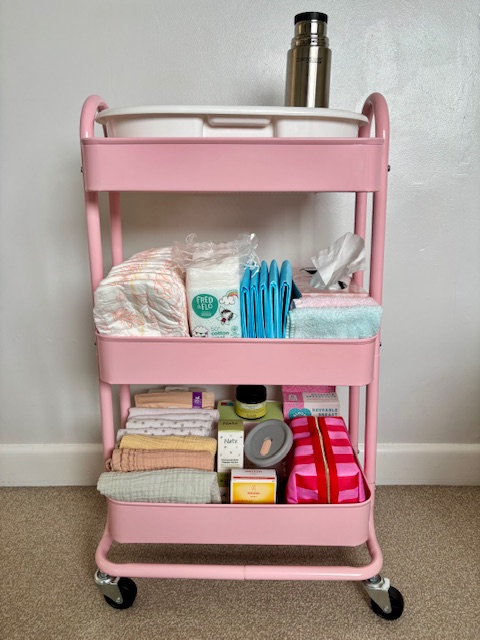 Pink 3 tiered trolley containing baby changing supplies.