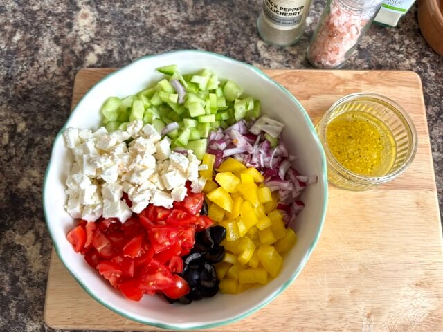 Greek Salad chopped up in a bowl next to the salad dressing